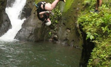 Person jumping into a waterfall pool.
