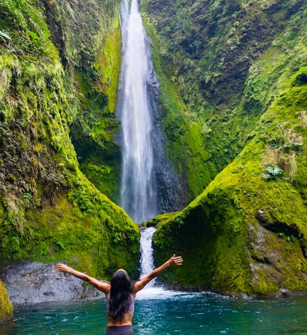 Person embracing nature by waterfall.