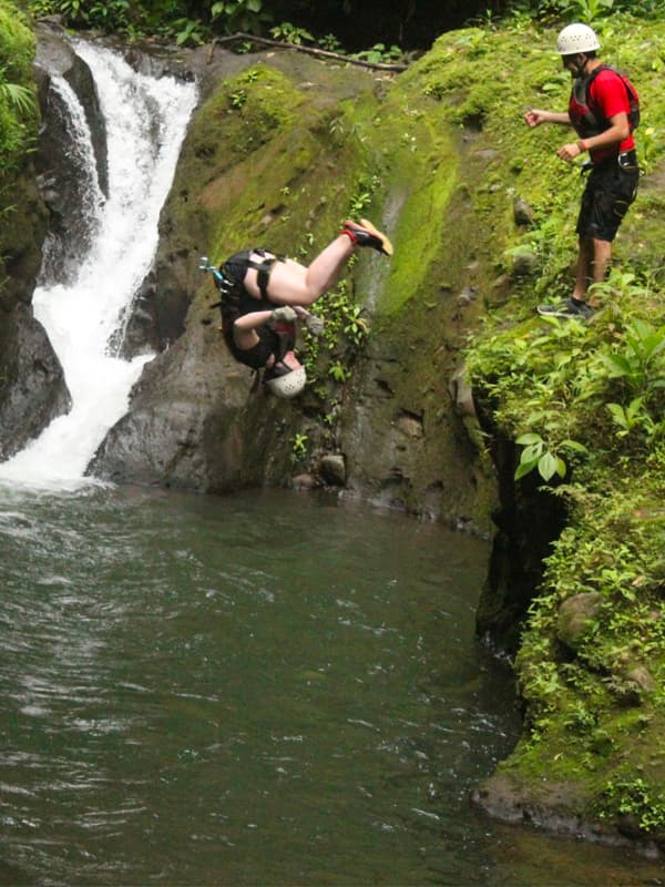 Person jumping into a waterfall pool.