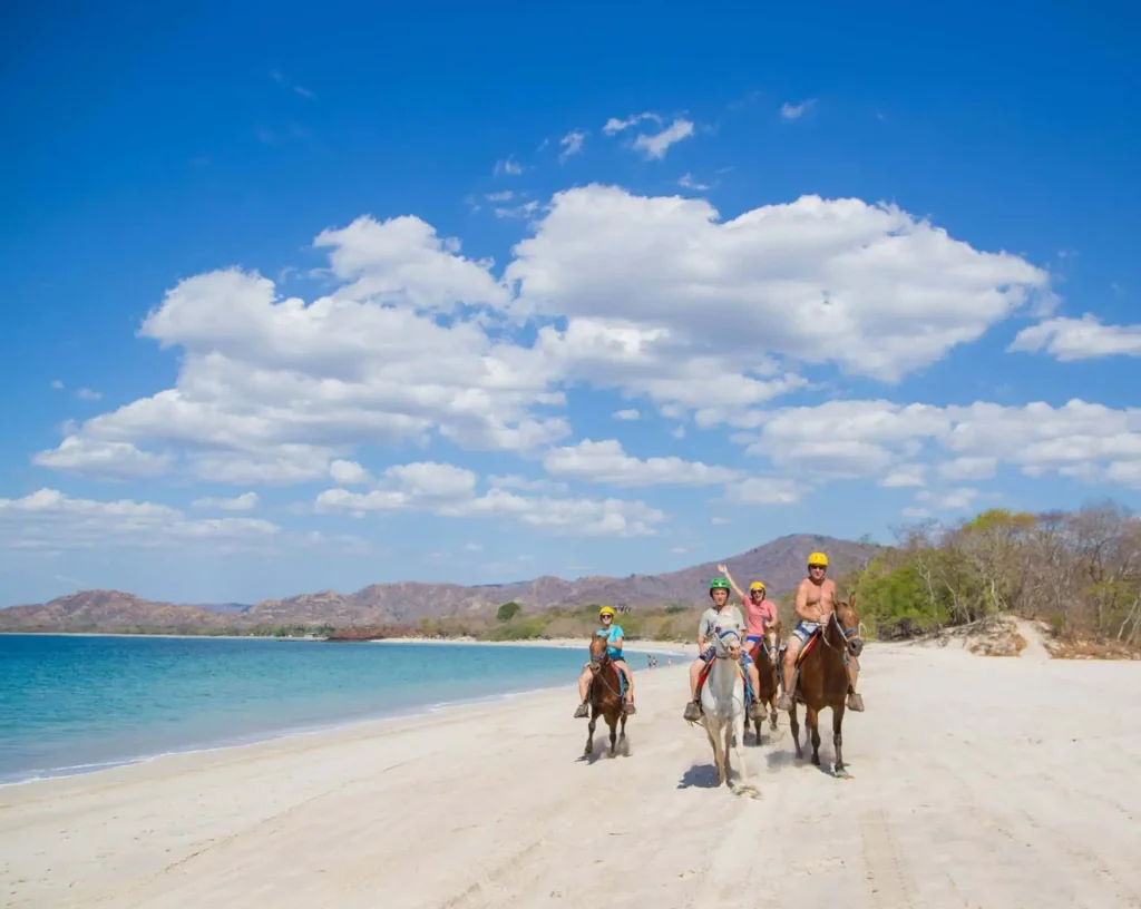People horseback riding on a beach.