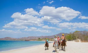 People horseback riding on a beach.
