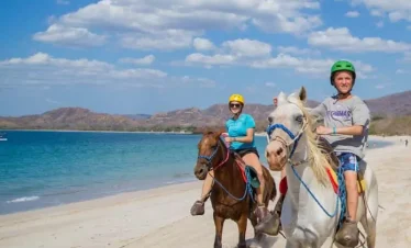 Two riders on horses by beach.